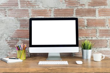 Boş beyaz ekranlı bilgisayar ve ahşap bir masada ofis malzemeleri olan çalışma alanı.