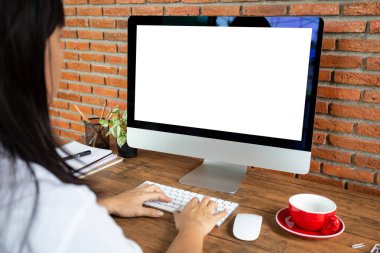 Genç bir kadın ofis odasındaki ahşap masada boş ekran bilgisayarda çalışıyor. kırpma yolu ile