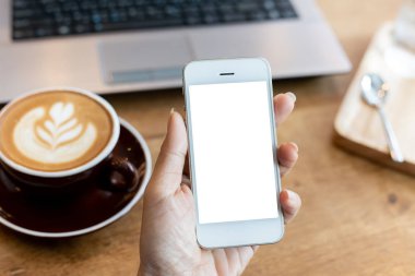 Telefon kullanan el kadını, kafeteryadaki boş ekran akıllı telefonu ve bilgisayarı ahşap masanın üzerinde. kırpma yolu ile