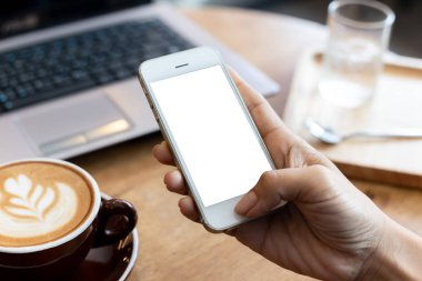 Telefon kullanan el kadını, kafeteryadaki boş ekran akıllı telefonu ve bilgisayarı ahşap masanın üzerinde. kırpma yolu ile