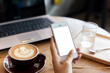 Telefon kullanan el kadını, kafeteryadaki boş ekran akıllı telefonu ve bilgisayarı ahşap masanın üzerinde. kırpma yolu ile