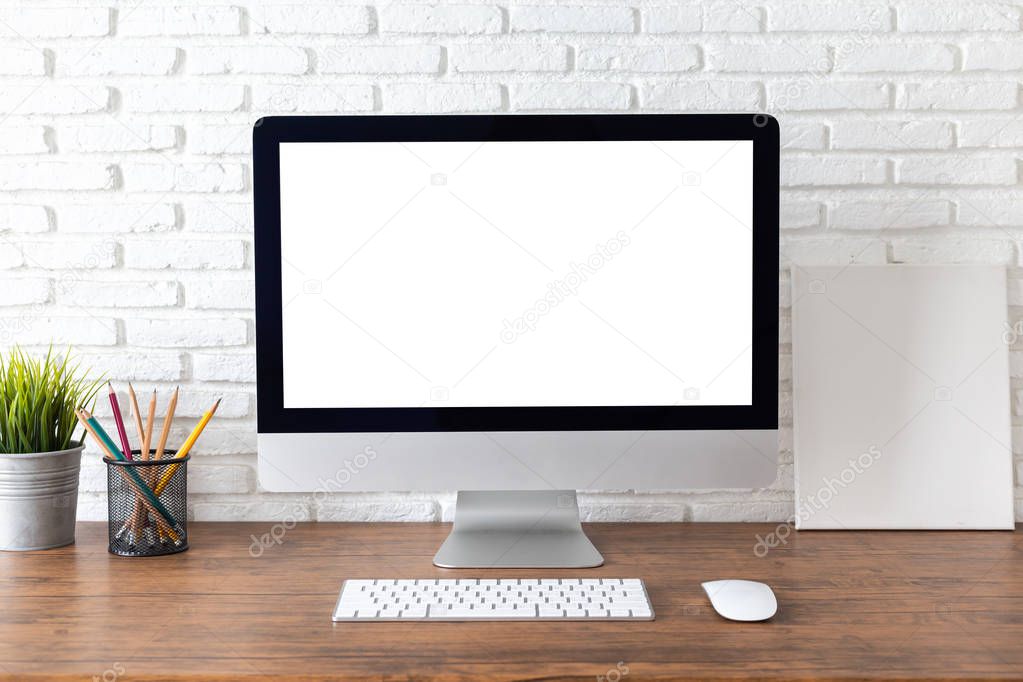 workspace with computer with blank white screen, and office supplies on a wooden desk