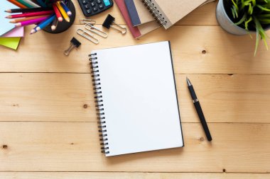 Üst manzara, boş defter ve ofis malzemeleri ahşap masada..