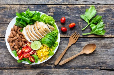 Sağlıklı yemek, sebze salatası, tavuk ve badem, ahşap bir masada beyaz bir tabakta. Üst görünüm