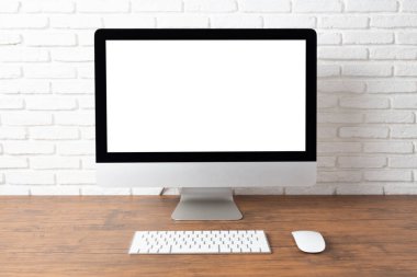 Boş beyaz ekranlı bilgisayar ve ahşap bir masada ofis malzemeleri olan çalışma alanı.