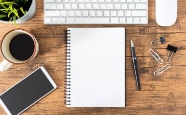 Masasında telefon ve bilgisayar olan boş bir defter.