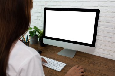 Kadın ev ofisteki ahşap masada boş ekran bilgisayarda çalışıyor.