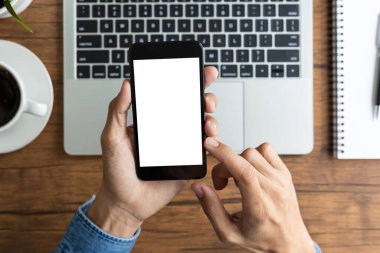 Üst düzey iş adamı elinde boş beyaz ekranlı akıllı telefon ve ahşap masada bilgisayar bilgisayarı tutuyor. 
