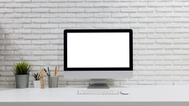 Boş beyaz ekranlı, çalışma alanı ve ofis malzemeleri olan bir bilgisayar.