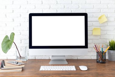 Boş beyaz ekranlı bilgisayar ve ahşap bir masada ofis malzemeleri olan çalışma alanı.