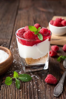 Üzerinde ahududu püresi ve ahşap arka planda taze böğürtlen olan cam bir kavanozda fırınlanmış cheesecake tatlısı yok.