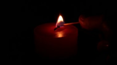 Adamın eli mutfak kibritiyle bir mum yakıyor. Kırmızı mum & tabak siyah arka plan üzerinde izole.