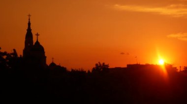 Kentsel çatılar, kilise ve ağaçların siluetleri üzerinde güzel gün batımı