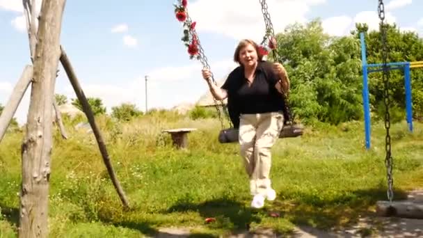 Ευτυχισμένη Ανώτερη Ξανθιά Γυναίκα Που Ταλαντεύεται Μια Ξύλινη Κούνια Καλοκαίρι — Αρχείο Βίντεο