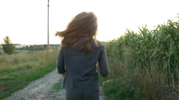 꼬리치는 소녀는 미소를 지으며 옥수수 근처의 도망가고 있습니다 일몰야외에서 스포츠 — 비디오