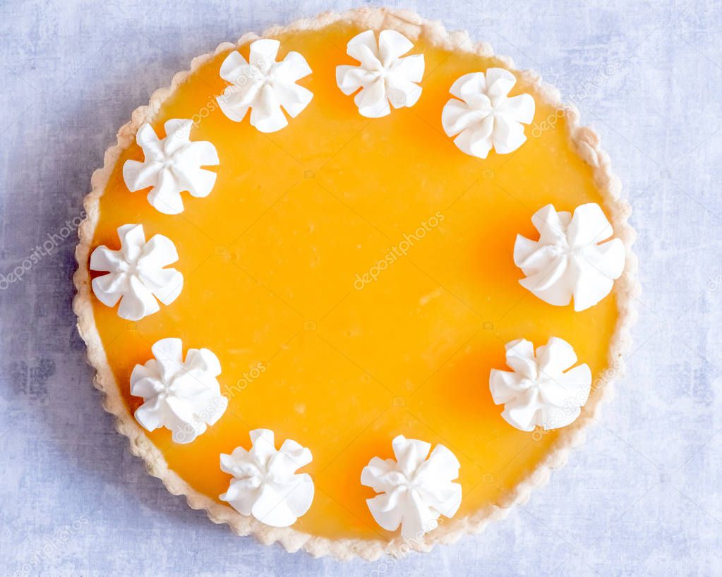 Top View Flat Lay of an Orange Jelly Passionfruit Tart with Whipped Cream Piped on the Outline over a Light Grey Background