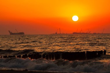 Baltık Denizi'nde gün batımı. Turuncu gökyüzü ve sörf.
