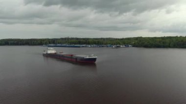 Açık ambarları olan büyük bir kargo gemisinin üzerinden uçmak ormanla çevrili sakin bir nehirde yelken açmak. Malları nehirden taşıyoruz. Güzel panoramik manzara. Üst görünüm aşağı