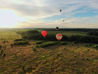 Yazın günbatımında mavi gökyüzünün arka planında yeşil bir tarla ve ormanın üzerinde balonlarla uçmak. İHA atışı
