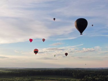 Yazın günbatımında mavi gökyüzünün arka planında yeşil bir tarla ve ormanın üzerinde balonlarla uçmak. İHA atışı