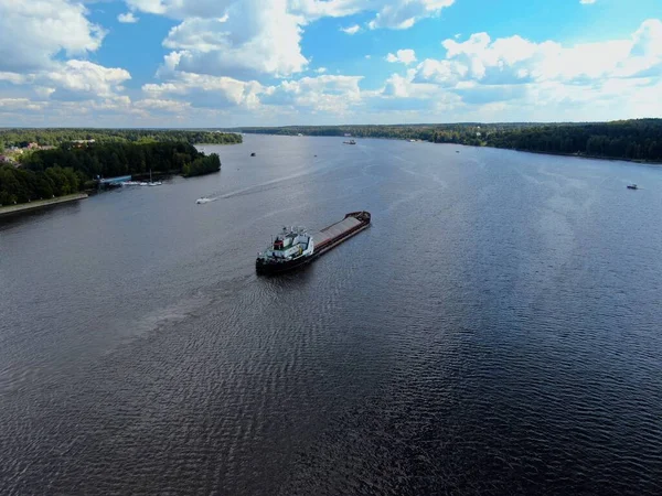 Aerial view cargo merchant ship sails along the river. Transport of goods by river barges. Beautiful landscape of the river.