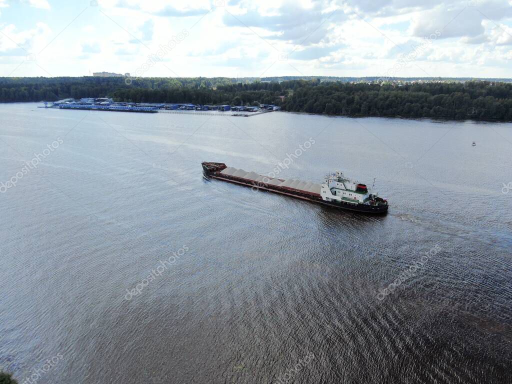 Aerial view cargo merchant ship sails along the river. Transport of goods by river barges. Beautiful landscape of the river.