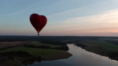 Hava manzaralı romantik balon uçuşu günbatımında büyük kırmızı bir kalp şeklinde. İnsansız hava aracının balonlarının izini sürdüğü güzel panoramik manzara uçuşları