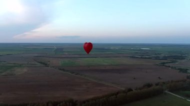 Hava manzaralı romantik balon uçuşu günbatımında büyük kırmızı bir kalp şeklinde. İnsansız hava aracının balonlarının izini sürdüğü güzel panoramik manzara uçuşları