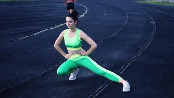 美丽的年轻女孩在绿色运动绑腿做热身腿在体育场 — 图库视频影像