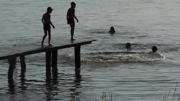 Siluetas Personas Corren Puente Atardecer Saltan Lago Más Cerca — Vídeos de Stock