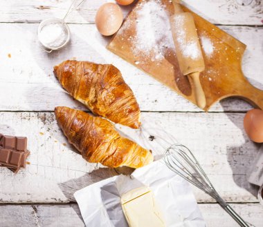 Pişmiş kruvasanlar ve pastane hazırlanması için malzemeler. Rustik tarzı. Beyaz ahşap zemin.