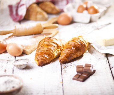 Pişmiş kruvasanlar ve pastane hazırlanması için malzemeler. Rustik tarzı. Beyaz ahşap zemin.