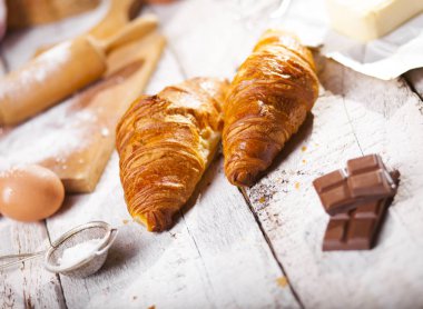 Pişmiş kruvasanlar ve pastane hazırlanması için malzemeler. Rustik tarzı. Beyaz ahşap zemin.