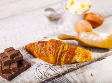 Pişmiş kruvasanlar ve pastane hazırlanması için malzemeler. Rustik tarzı. Beyaz ahşap zemin.