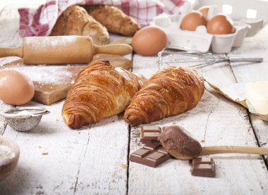 Pişmiş kruvasanlar ve pastane hazırlanması için malzemeler. Rustik tarzı. Beyaz ahşap zemin.