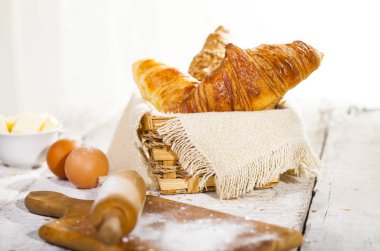 Pişmiş kruvasanlar ve pastane hazırlanması için malzemeler. Rustik tarzı. Beyaz ahşap zemin.