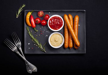 Wiener sosis siyah arka plan üzerine bir tabak içinde baharatlar ile. Kopya alanı ile üstten görünüm.