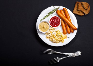 Wiener sosis ve siyah arka plan üzerine bir tabak içinde baharatlar ile pişmiş yumurta. Kopya alanı ile üstten görünüm.