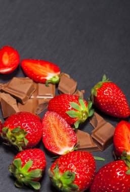 Yaprakları ve kopya alanı siyah zemin üzerine çikolata parçaları ile taze sulu çilek.