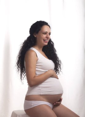 Beyaz yelek ve bikini beyaz bir arka plan üzerinde olan hamile bir kadın portresi.