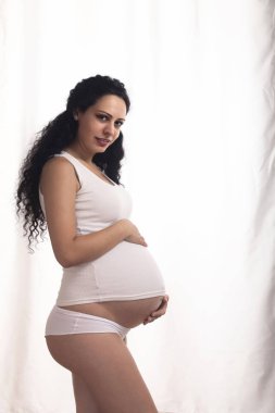 Beyaz yelek ve bikini beyaz bir arka plan üzerinde olan hamile bir kadın portresi.