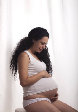 Beyaz yelek ve bikini beyaz bir arka plan üzerinde olan hamile bir kadın portresi.