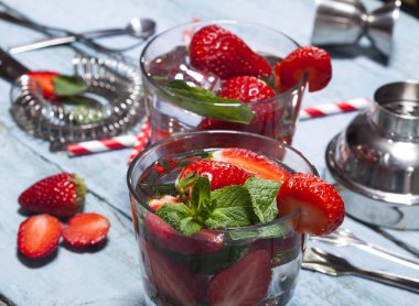 Çilek, nane ve buz cam mavi ahşap zemin üzerine yaz soğuk içecek. Kokteyl bar araçları ile taze berry meyve yapma.