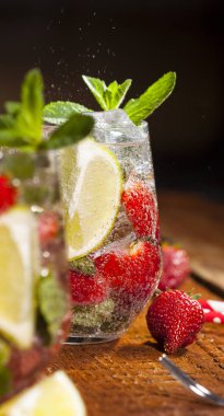 Çilek, nane, limon ve buz cam üstünde ahşap bar sayaç ile yaz soğuk içecek. Closeup taze berry meyve kokteyli.