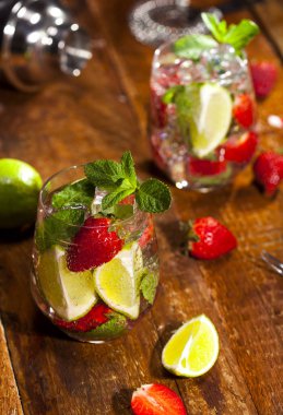 Çilek, nane, limon ve buz cam üstünde ahşap bar sayaç ile yaz soğuk içecek. Closeup taze berry meyve kokteyli.