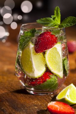 Çilek, nane, limon ve buz cam üstünde ahşap bar sayaç ile yaz soğuk içecek. Closeup taze berry meyve kokteyli.