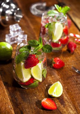Çilek, nane, limon ve buz cam üstünde ahşap bar sayaç ile yaz soğuk içecek. Closeup taze berry meyve kokteyli.