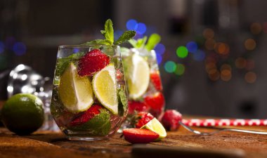 Çilek, nane, limon ve buz cam üstünde ahşap bar sayaç ile yaz soğuk içecek. Closeup taze berry meyve kokteyli.