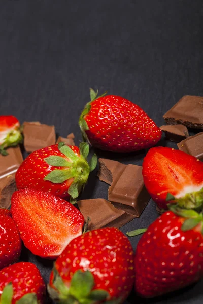 Yaprakları ve kopya alanı siyah zemin üzerine çikolata parçaları ile taze sulu çilek.