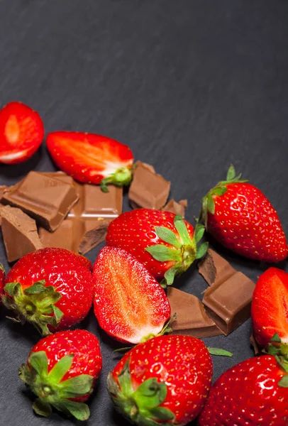 Yaprakları ve kopya alanı siyah zemin üzerine çikolata parçaları ile taze sulu çilek.